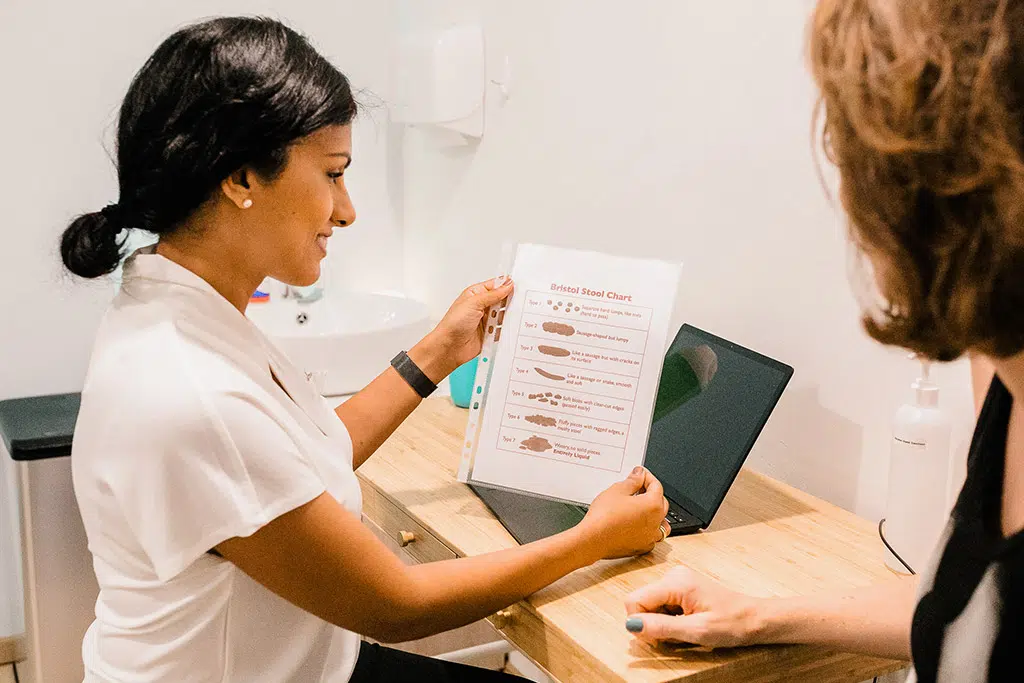 A physiotherapist explaining a pelvic health chart to a client at a desk